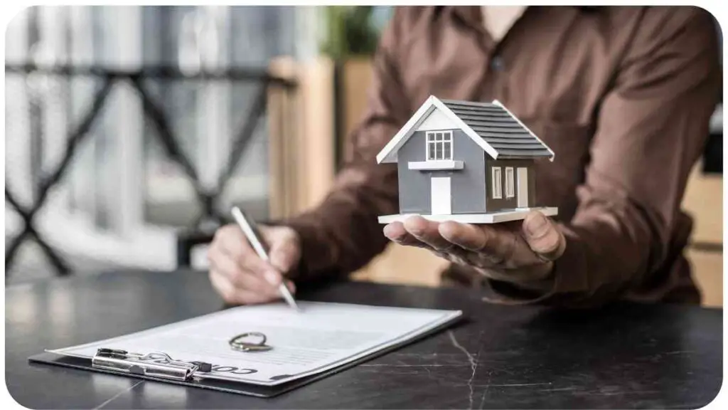 man holding a house model on a table with a pen and paper in front of them