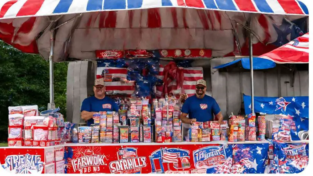 two individuals stand under an american flag tent selling fireworks