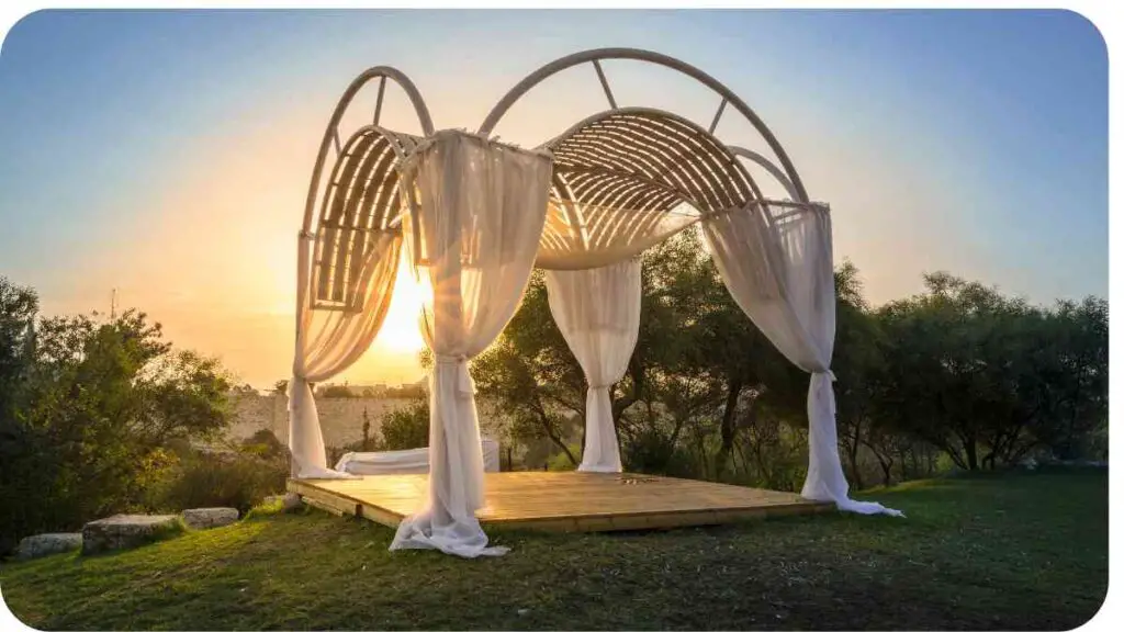a gazebo with white drapes on it at sunset